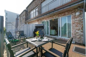 Une terrasse extérieure avec une table pour deux, un barbecue et un coin salon avec des chaises.