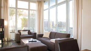 Un soggiorno moderno con un divano componibile, un tavolino in vetro e una TV su un mobile. Ampie finestre offrono una vista sulla città.