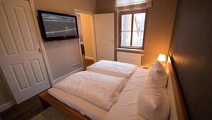 A bedroom with a bed, a TV mounted on the wall, a window with a view of buildings, and a door. - Rainer Maria Rilke apartment in the author's house on Usedom! - Author's House Usedom (Heringsdorf)
