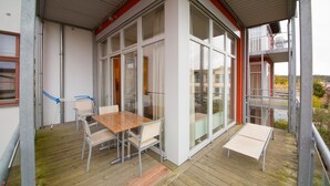 A modern outdoor patio with a wooden table and chairs, large glass windows, and a balcony. - Rainer Maria Rilke apartment in the author's house on Usedom! - Author's House Usedom (Heringsdorf)