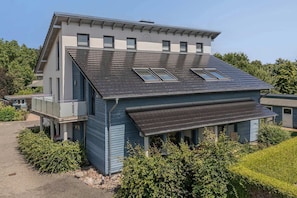 A modern two-story house with a sloped roof, multiple windows, and a covered porch area.