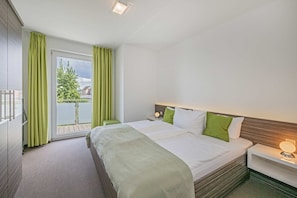 A hotel room with a bed, a nightstand, a window with curtains, and a view of greenery outside.