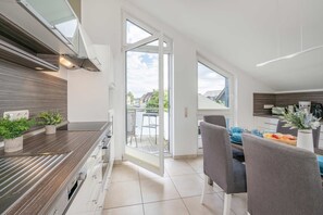 A modern kitchen with a built-in oven, a dining area with a table and chairs, and a view of the outdoors through large windows.