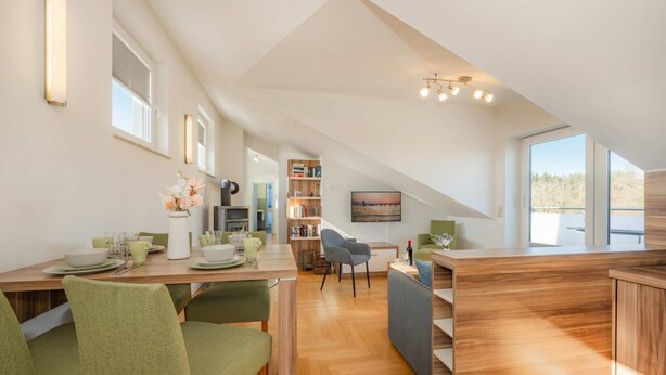 Un interior moderno con comedor, cocina y sala de estar, destacando un techo alto y ventanas amplias.