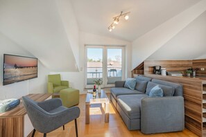 Una sala de estar moderna con un sofá, sillas, un televisor y una cocina con armarios de madera.