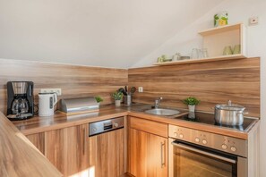 A modern kitchen with wooden cabinets, a built-in oven, a coffee maker, and a sink.