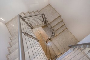 Una escalera de caracol con barandillas de metal y peldaños de baldosas color beige.