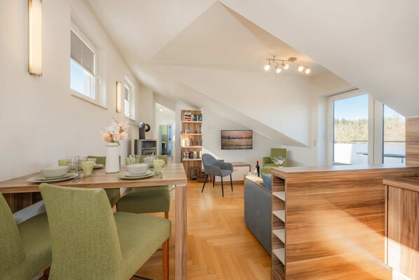 Un interior moderno con comedor, cocina y sala de estar, destacando un techo alto y ventanas amplias.