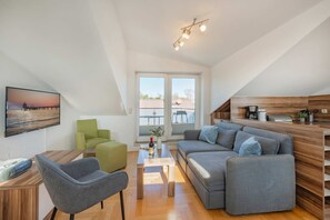Una sala de estar moderna con un sofá, sillas, un televisor y una cocina con armarios de madera.