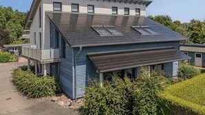 Una casa moderna de dos pisos con techo inclinado, múltiples ventanas y un porche cubierto.
