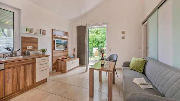 A modern kitchen with wooden cabinets, a dining area with a table and chairs, and a grey sofa with a green pillow. - Cozy vacation apartment in Zinnowitz with terrace and garden on Usedom - House (Zinnowitz)