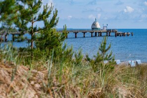 A coastal scene with a pier, a dome-like structure, and beach chairs. - Cozy vacation apartment in Zinnowitz with terrace and garden on Usedom - House (Zinnowitz)