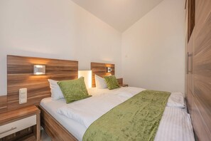 Un dormitorio con cabecera de madera, dos mesitas de noche con lámparas, cama con ropa de cama blanca y almohadones verdes, y una manta verde.