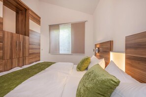 A bedroom with two beds, wooden headboards, a window with blinds, and a green throw on the beds.