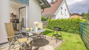 A patio with a table and chairs, a grill, and a view of a house with a white exterior and a red roof. - Cozy vacation apartment in Zinnowitz with terrace and garden on Usedom - House (Zinnowitz)