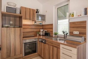 A modern kitchen with wooden cabinetry, a microwave, a toaster, and a built-in oven. - Cozy vacation apartment in Zinnowitz with a terrace and garden on Usedom - House (Zinnowitz)