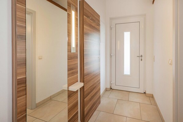 A hallway with a wooden accent wall, a white door with a window, and a white shelf.