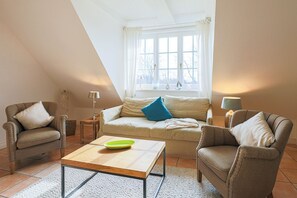 Ett mysigt vardagsrum med en soffa, två fåtöljer, ett soffbord och en lampa.