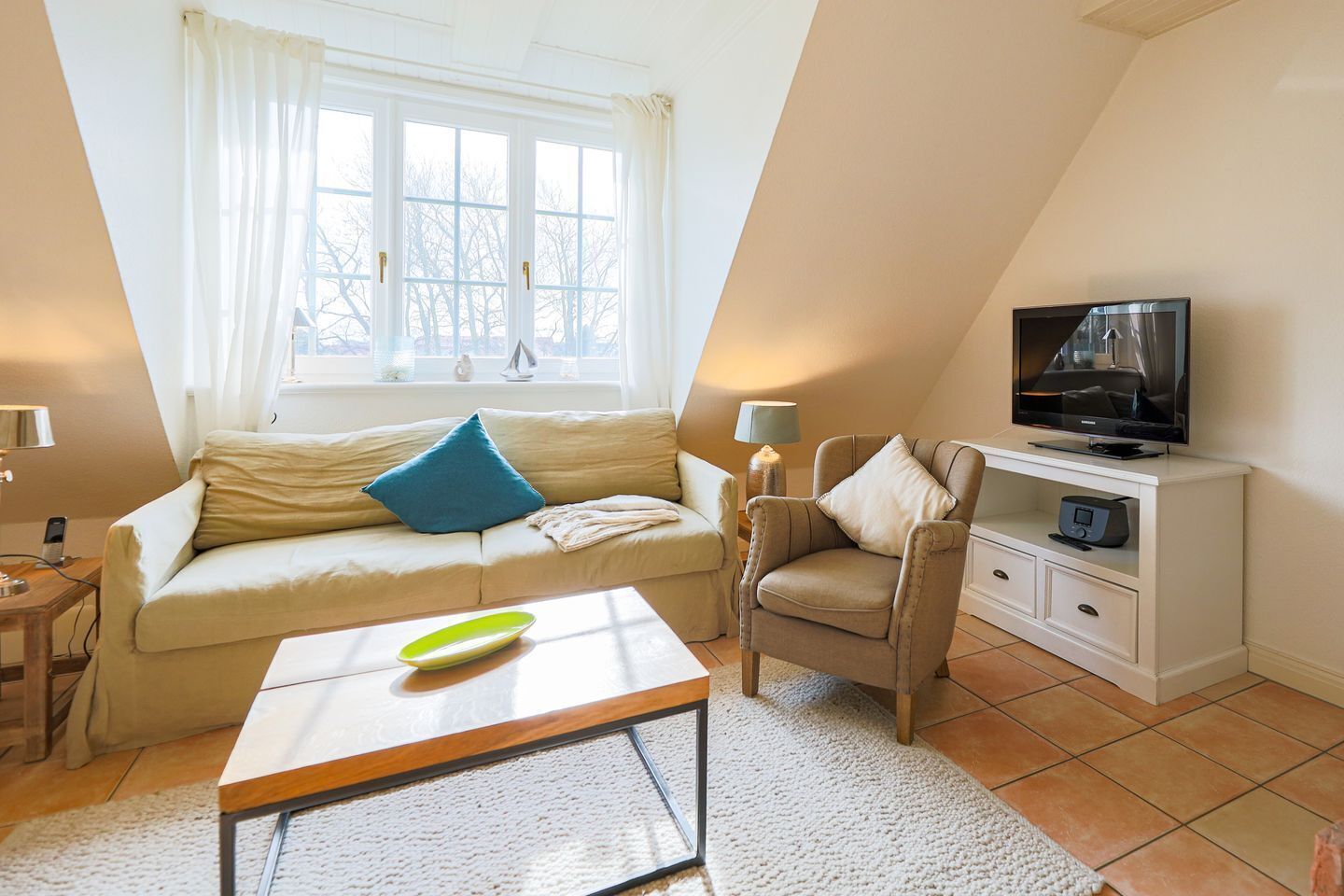 Ein gemütliches Wohnzimmer mit Sofa, Sessel, Couchtisch und einem Fernseher auf einem Schrank.