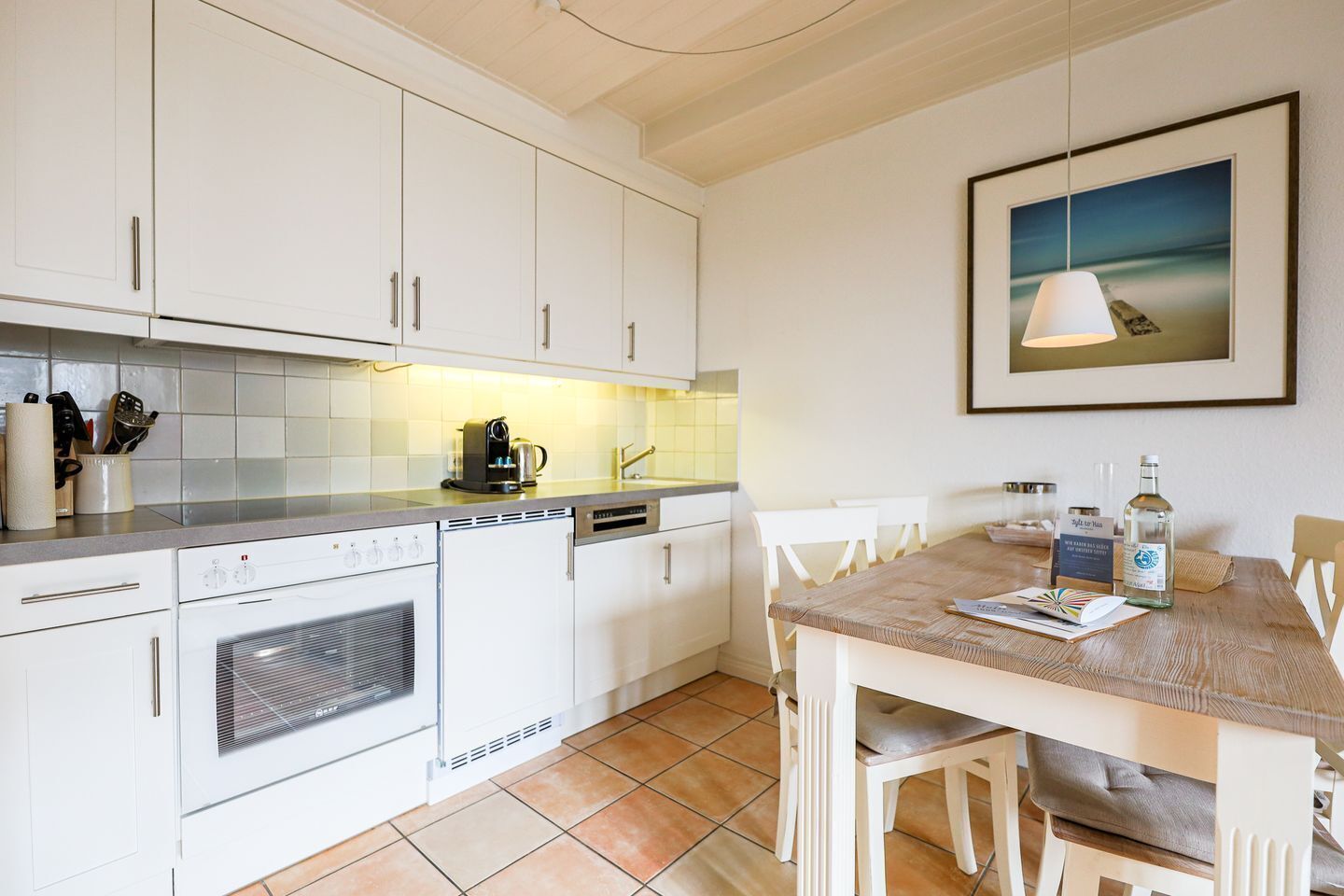 Una cucina moderna con mobili bianchi, un tavolo da pranzo in legno e un quadro appeso sopra il tavolo.