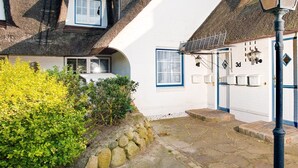 A traditional white building with a thatched roof, stone steps, and a small garden with yellow foliage.