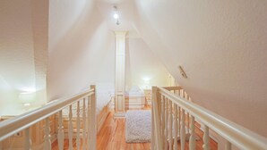 A staircase with white railings leading to a bedroom with a bed, a nightstand, and a lamp.