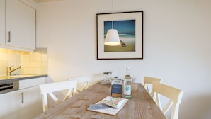 A dining area with a wooden table, white chairs, a framed picture on the wall, and a bottle of water.
