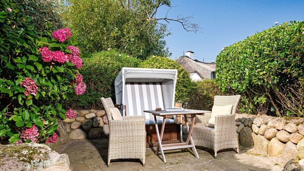 An outdoor seating area with wicker chairs and a table, surrounded by stone walls and lush greenery.