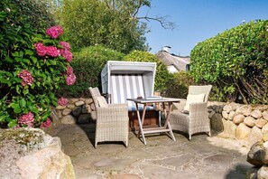 An outdoor seating area with wicker chairs and a table, surrounded by stone walls and lush greenery. - Lisbeth Hus - Ameland Station - Lisbeth Hus at Ameland Station (Wenningstedt-Braderup (Sylt))