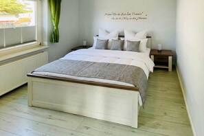 Une chambre à coucher avec un lit, des tables de chevet, une fenêtre avec des rideaux et un mur sur lequel est affiché un message.