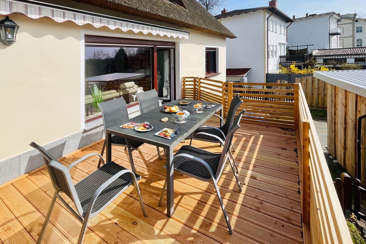 Un espace extérieur aménagé pour les repas, avec une table dressée pour quatre personnes, entourée de chaises, sur une terrasse en bois dotée d’une rambarde.