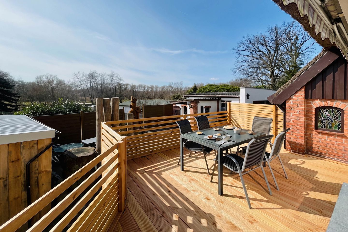 An outdoor patio with a table and chairs, a wooden deck, and a brick wall with a window.