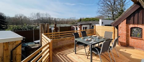 An outdoor patio with a table and chairs, a wooden deck, and a brick wall with a window.
