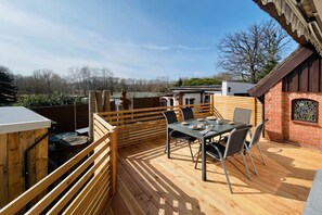Une terrasse extérieure avec une table et des chaises, une terrasse en bois et un mur de briques agrémenté d’une fenêtre.