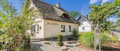 A traditional building with a thatched roof, a sign reading 'Unser Schloss,' and a well-maintained garden with gravel paths and greenery.