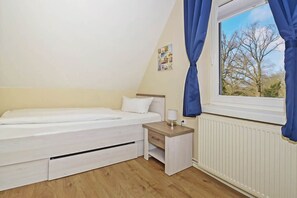 A bedroom with a single bed, a bedside table with a lamp, a window with curtains, and a radiator.