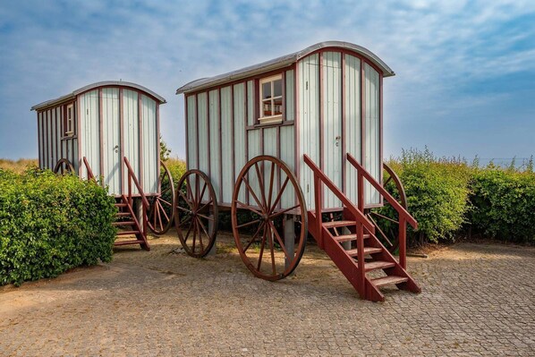 Two wooden structures with large wheels and stairs, surrounded by greenery.