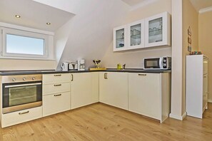 A kitchen with white cabinets, a microwave, and a window above the oven. - Modern vacation apartment in Heringsdorf with a terrace—100 m from the beach on Usedom (Heringsdorf)