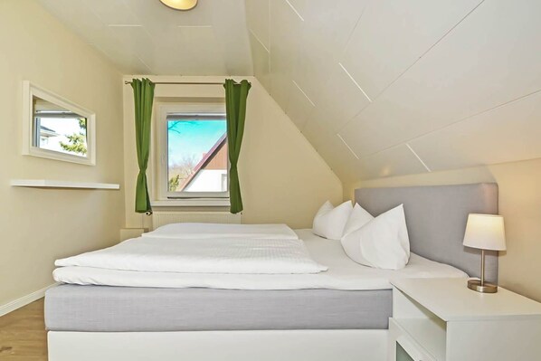 Une chambre à coucher avec un lit, une table de chevet, une lampe, une fenêtre avec des rideaux et une vue sur l’extérieur.