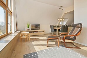 Un salon moderne comprenant un coin repas, un plancher en bois, un téléviseur et une grande fenêtre.