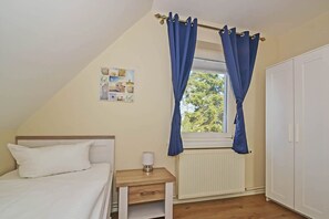 Une chambre à coucher comprenant un lit, une table de chevet, une fenêtre avec des rideaux, un radiateur et une armoire.