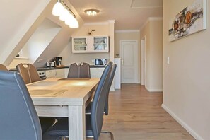 A dining area with a long table, chairs, and a kitchen in the background.