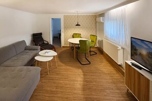En moderne stue med sofa, spisebord med stole, fjernsyn og en radiator.