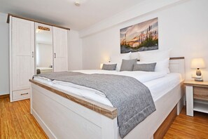 Une chambre à coucher avec un lit, une table de chevet, une lampe, une armoire et un tableau accroché au mur.