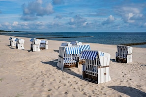 Strandstole med nummer på stranden, en klar himmel og havet i baggrunden.