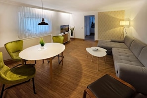 Un salon moderne avec une table ronde, des chaises vertes, un canapé gris et une petite table blanche.