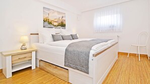 Ein Schlafzimmer mit einem Bett, einem Nachttisch, einem Sessel und einem Fenster mit Vorhängen.