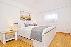 Une chambre à coucher avec un lit, une table de chevet, une chaise et une fenêtre avec des rideaux.