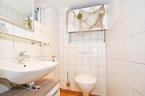 Une salle de bain avec un lavabo blanc, des toilettes et un miroir.