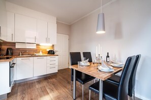 Uma cozinha moderna com armários brancos, bancada de madeira e uma área de jantar com mesa para quatro pessoas.